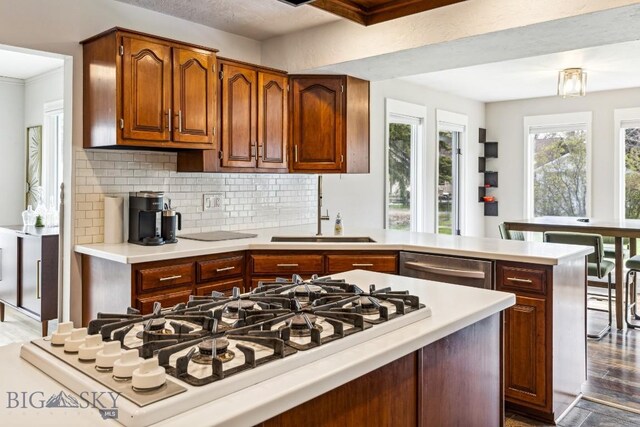 kitchen with a sink, white gas cooktop, light countertops, and decorative backsplash