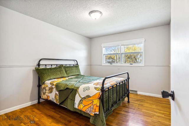 bedroom with wood finished floors, a textured ceiling, baseboards, and a baseboard heating unit