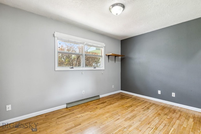 unfurnished room featuring a baseboard radiator, wood finished floors, baseboards, and a textured ceiling