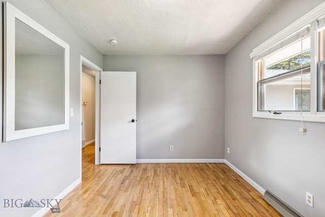 spare room with a baseboard radiator, light wood-type flooring, baseboards, and a smoke detector