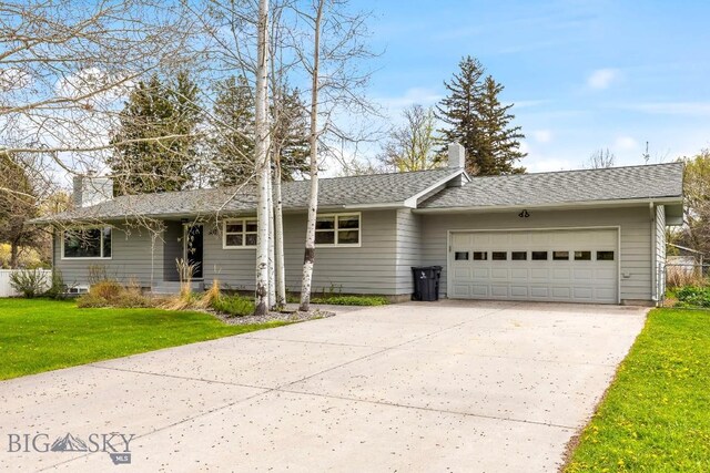 ranch-style house with a chimney, a garage, a front yard, driveway, and roof with shingles