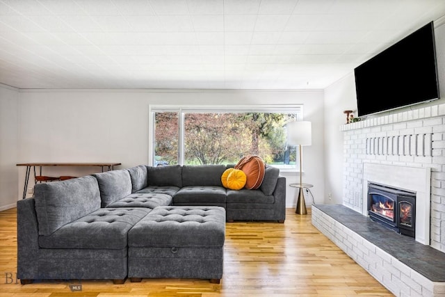 living area featuring crown molding, a brick fireplace, and light wood-style floors