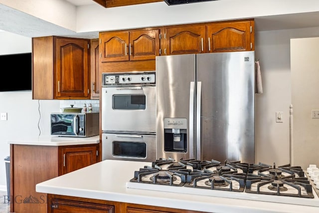 kitchen with appliances with stainless steel finishes, brown cabinets, and light countertops