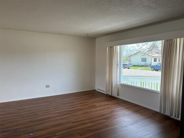 spare room featuring dark wood-style flooring, healthy amount of natural light, a textured ceiling, and baseboards