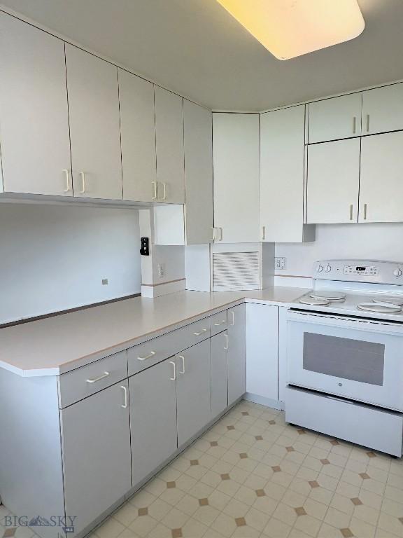 kitchen featuring electric range, light countertops, and white cabinetry