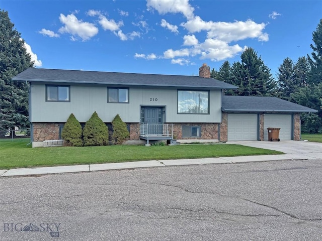 raised ranch with a garage, a chimney, a front lawn, concrete driveway, and stone siding