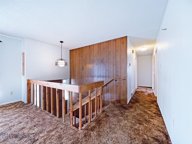 corridor featuring carpet, wooden walls, an upstairs landing, a textured ceiling, and baseboards
