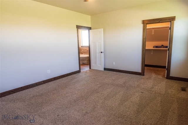 unfurnished bedroom with a walk in closet, carpet floors, and baseboards