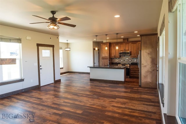 kitchen with appliances with stainless steel finishes, dark countertops, brown cabinetry, ceiling fan, and tasteful backsplash