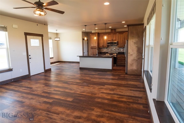 kitchen featuring stainless steel appliances, dark countertops, brown cabinetry, decorative backsplash, and a ceiling fan