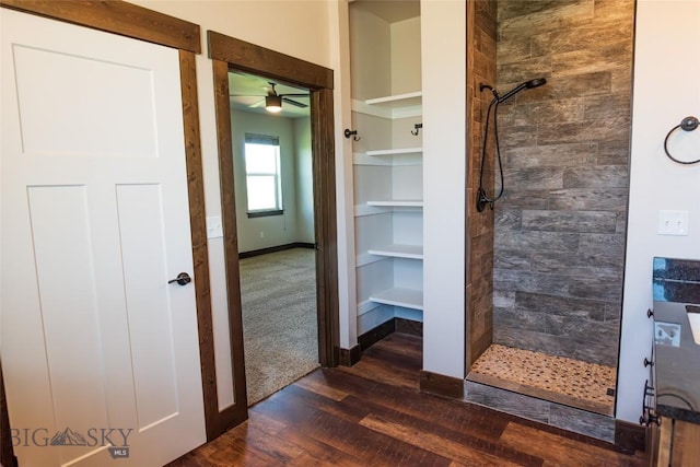 full bath featuring tiled shower, wood finished floors, ceiling fan, and baseboards