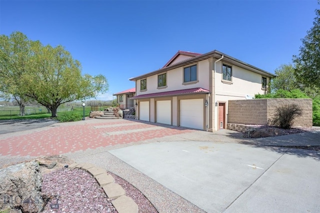 view of side of home featuring stucco siding, driveway, an attached garage, and fence