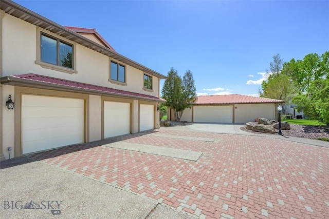 view of front of home with stucco siding, decorative driveway, a garage, and a tile roof