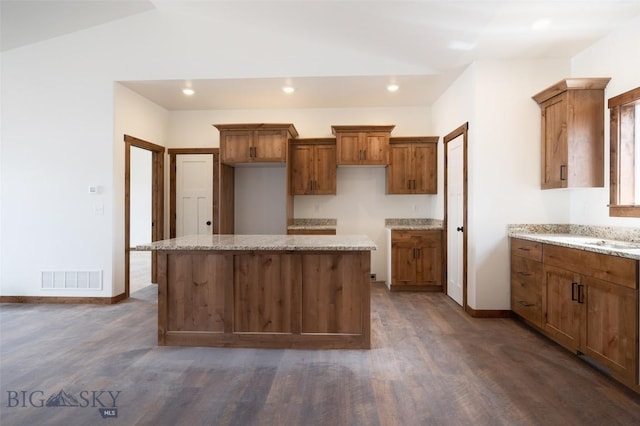 kitchen with brown cabinetry, dark wood-style floors, a kitchen island, recessed lighting, and vaulted ceiling
