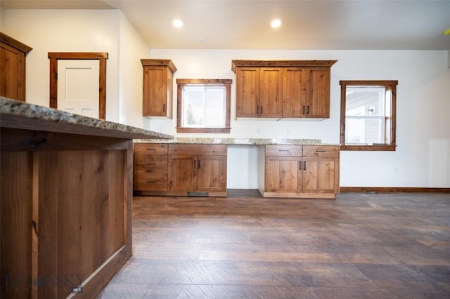kitchen with dark wood finished floors, brown cabinetry, light stone counters, baseboards, and recessed lighting