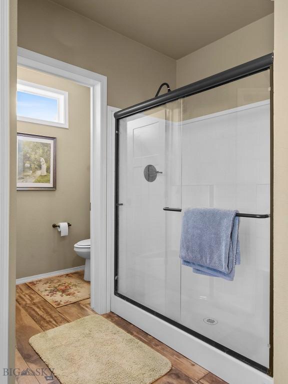 bathroom with a shower stall, toilet, wood finished floors, and baseboards