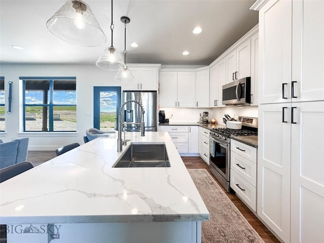 kitchen with appliances with stainless steel finishes, a sink, dark wood-style flooring, a kitchen island with sink, and white cabinetry