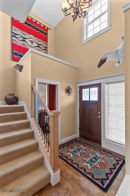 foyer entrance featuring a chandelier, a towering ceiling, stairs, wood finished floors, and baseboards