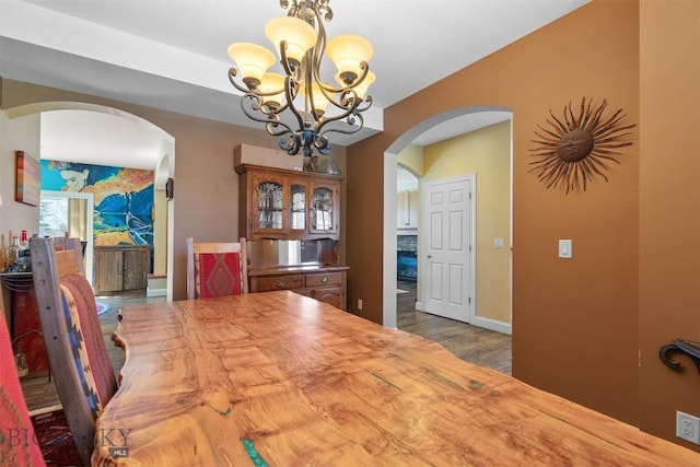 dining space featuring arched walkways, a chandelier, wood finished floors, and baseboards