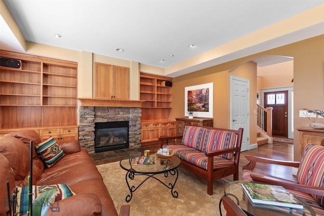 living room featuring arched walkways, a stone fireplace, stairway, baseboards, and recessed lighting