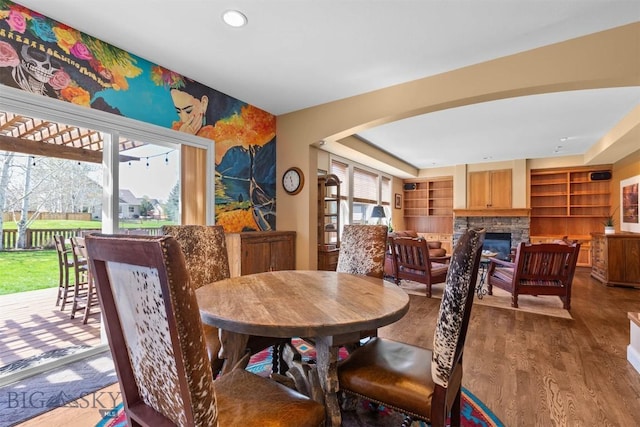 dining room featuring a stone fireplace, wood finished floors, built in features, and recessed lighting