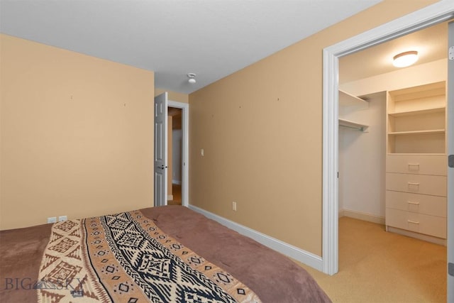 bedroom featuring light carpet, a spacious closet, a closet, and baseboards