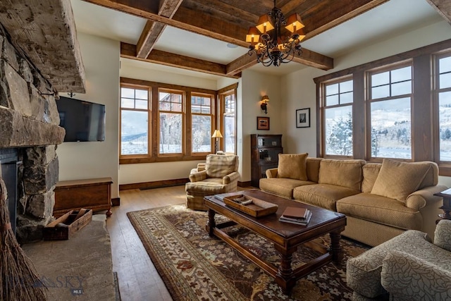 living area with hardwood / wood-style flooring, a stone fireplace, beamed ceiling, a chandelier, and baseboards