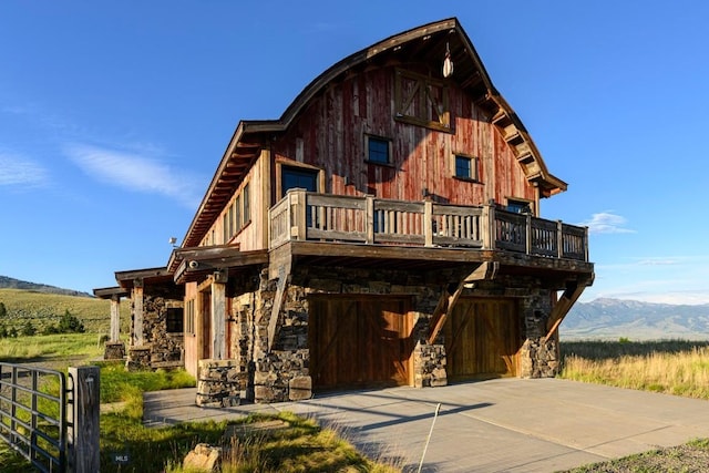 view of front of property with stone siding, driveway, a mountain view, a balcony, and a garage