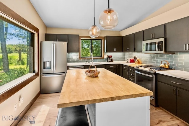 kitchen featuring appliances with stainless steel finishes, wooden counters, a sink, decorative backsplash, and hanging light fixtures