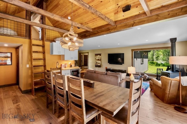 dining space featuring light wood finished floors, wine cooler, beam ceiling, a chandelier, and wood ceiling