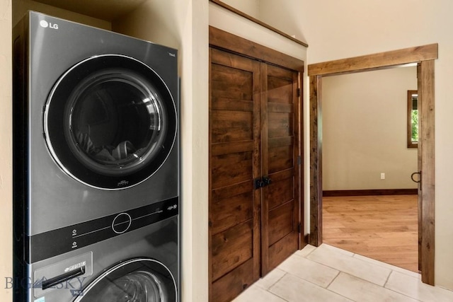 laundry room featuring stacked washer and clothes dryer, light tile patterned flooring, and baseboards