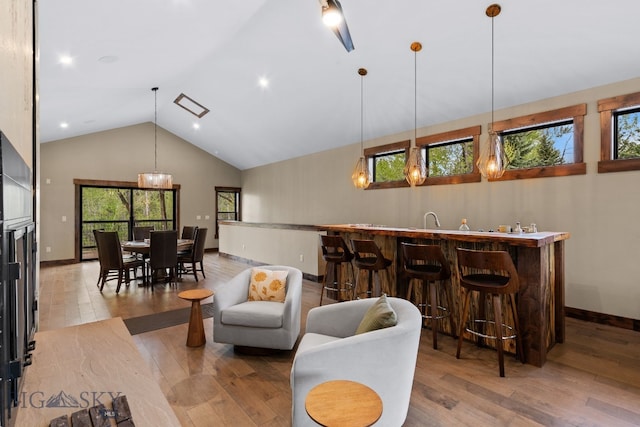 living area with light wood-type flooring, plenty of natural light, bar with sink, and high vaulted ceiling