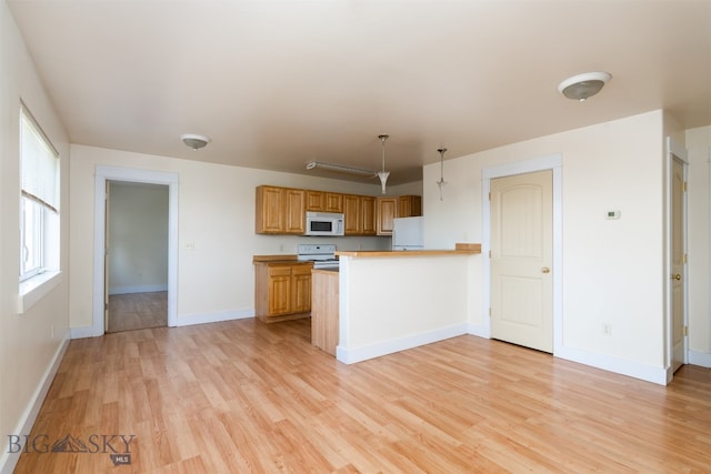 kitchen featuring white appliances, light wood finished floors, a peninsula, and baseboards