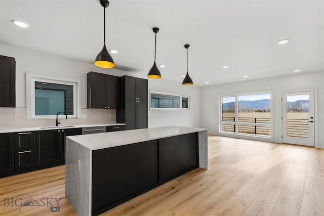 kitchen with a sink, dark cabinets, light wood-type flooring, decorative backsplash, and recessed lighting