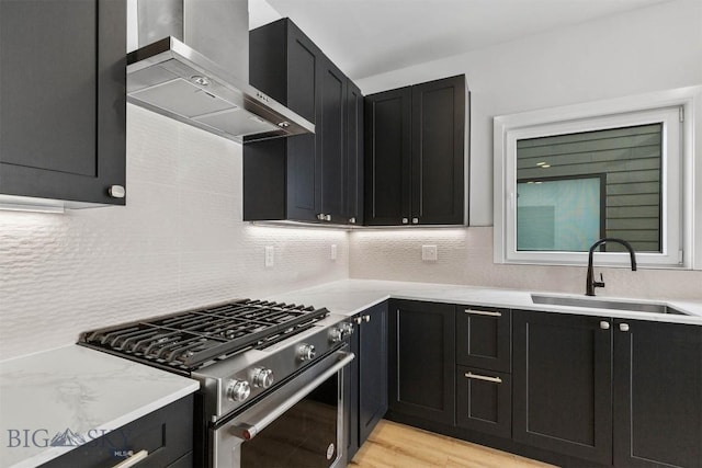 kitchen featuring gas range, a sink, dark cabinets, and wall chimney range hood