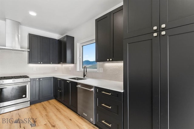 kitchen with stainless steel appliances, wall chimney range hood, a sink, light countertops, and backsplash