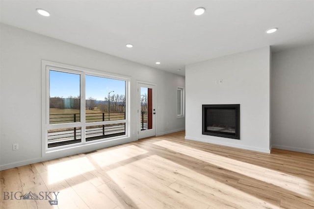 unfurnished living room with baseboards, wood finished floors, a glass covered fireplace, and recessed lighting