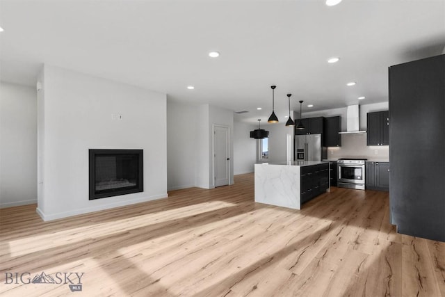 kitchen with appliances with stainless steel finishes, wall chimney range hood, a center island, light wood-style floors, and recessed lighting