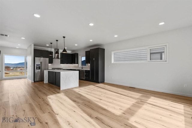 kitchen with stainless steel fridge with ice dispenser, a center island, dark cabinets, light wood-type flooring, and open floor plan
