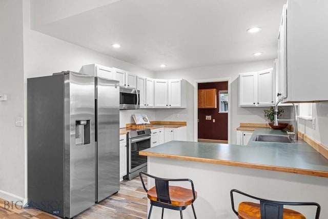 285 Hereford Dr, Belgrade, MT 59714 - kitchen with appliances with stainless steel finishes, a peninsula, light wood-style floors, a kitchen breakfast bar, and white cabinetry