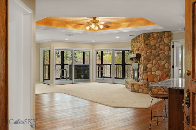 unfurnished living room featuring a raised ceiling, wood finished floors, crown molding, ceiling fan, and a fireplace