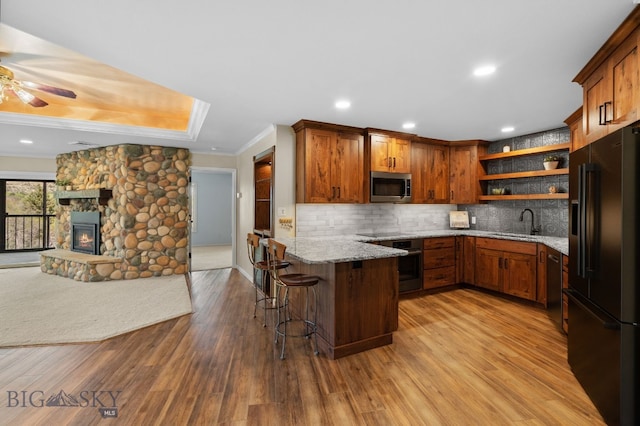 kitchen with appliances with stainless steel finishes, a peninsula, open shelves, open floor plan, and a sink