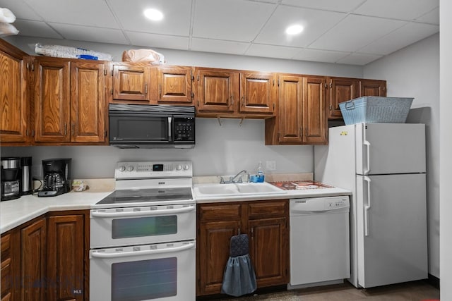 kitchen with white appliances, a sink, light countertops, a paneled ceiling, and brown cabinetry