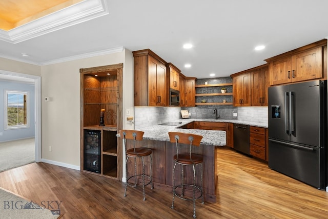kitchen with appliances with stainless steel finishes, open shelves, beverage cooler, wood finished floors, and light stone counters