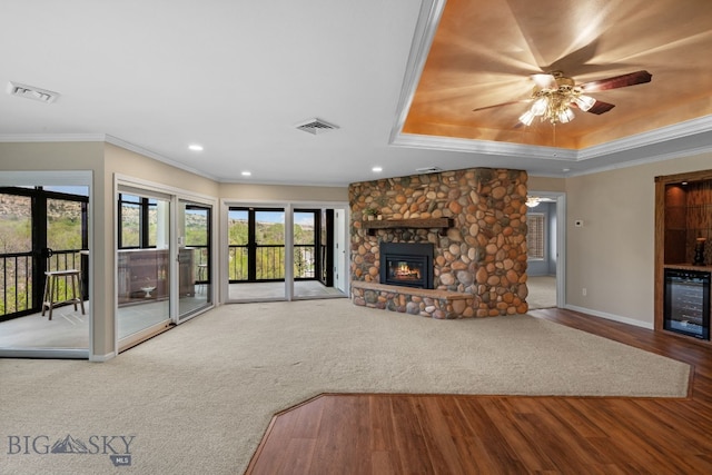 unfurnished living room with wine cooler, ornamental molding, a raised ceiling, a fireplace, and baseboards