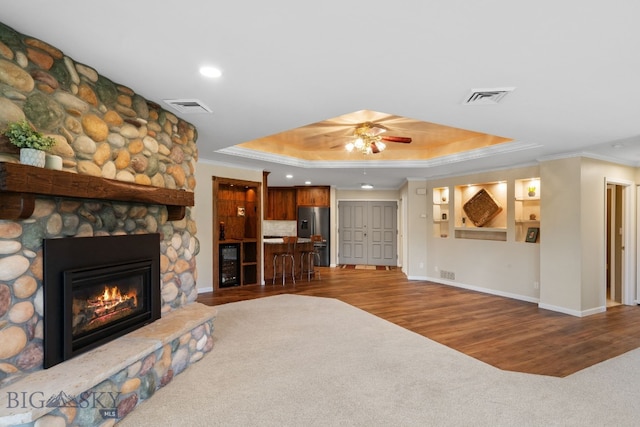 living room featuring a raised ceiling, ornamental molding, a ceiling fan, baseboards, and wood finished floors