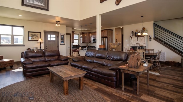 living room featuring dark wood-style flooring, stairs, and a chandelier