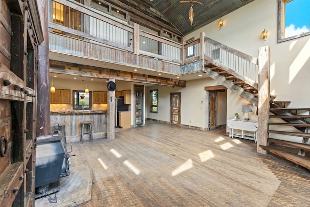 unfurnished living room featuring high vaulted ceiling, stairway, a wood stove, light carpet, and baseboards
