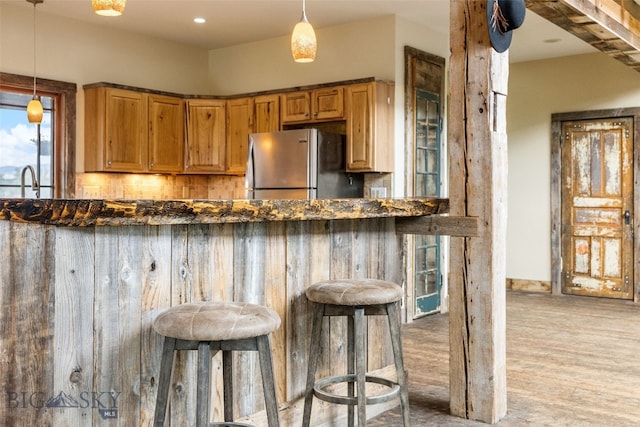kitchen with freestanding refrigerator, a breakfast bar, light wood-type flooring, pendant lighting, and dark stone counters