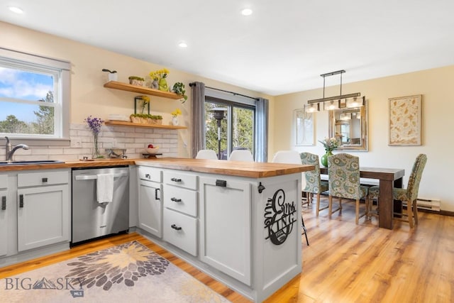 kitchen featuring dishwasher, butcher block countertops, a sink, backsplash, and light wood-style flooring